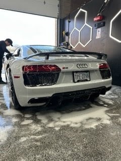 White Audi R8 sports car being washed in an indoor garage with geometric wall art visible