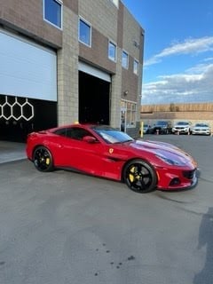 Red sports car parked in front of a modern concrete building with large windows and metal garage door