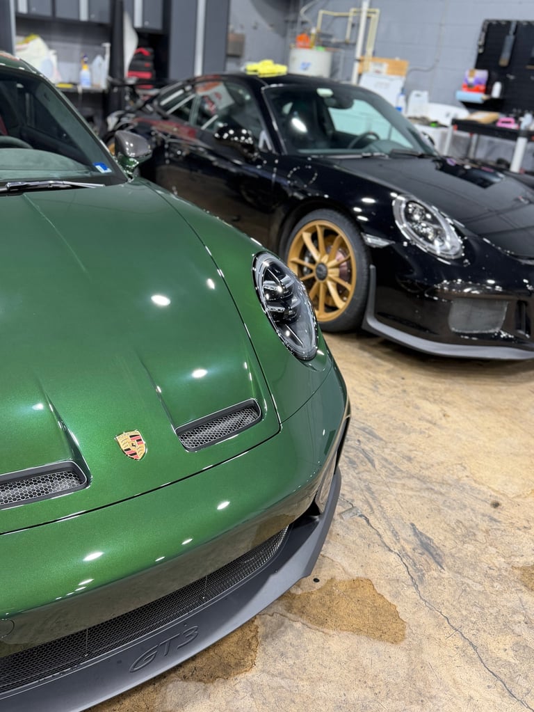 Green and black Porsche sports cars parked in an indoor garage showroom