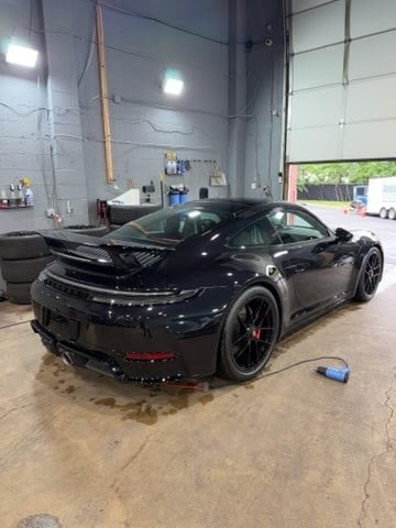 Black Porsche sports car in automotive garage with concrete floor and industrial ceiling