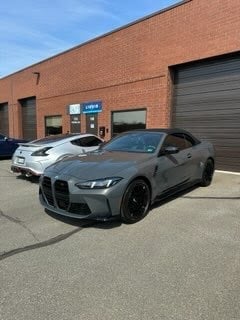 Gray BMW M440i parked in front of brick building with other cars visible in background