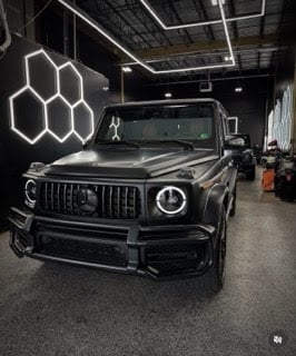 Black Mercedes-AMG G-Class SUV displayed in modern garage with hexagonal neon sign overhead