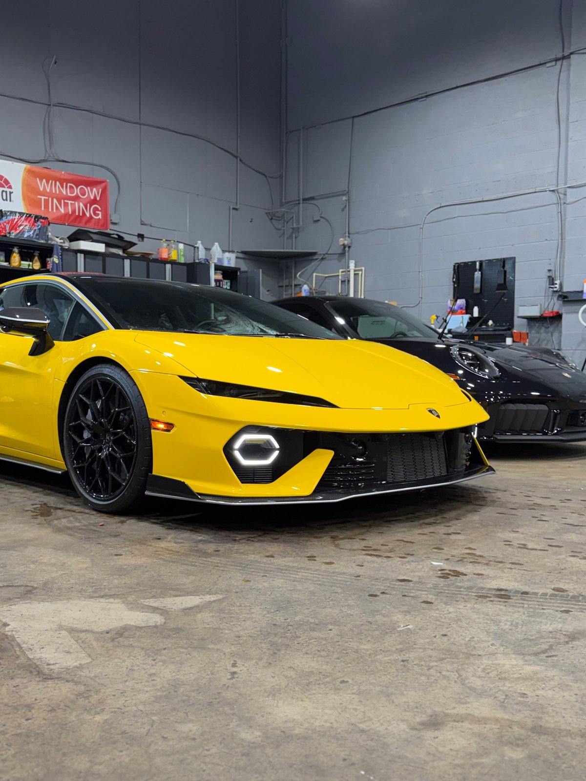 Bright yellow sports car with circular headlights parked in an auto shop next to a black vehicle