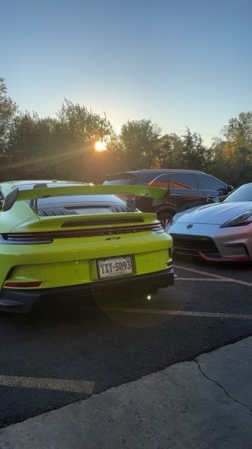Row of luxury sports cars parked in a lot during sunset, including a bright yellow Porsche in the foreground