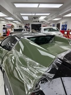 Green sports car with protective plastic wrap in an indoor automotive service facility