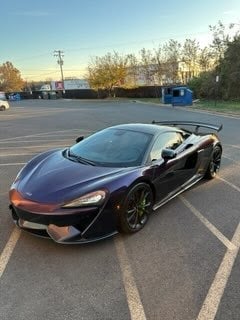 Black sports car parked in lot with commercial buildings and utility pole in background