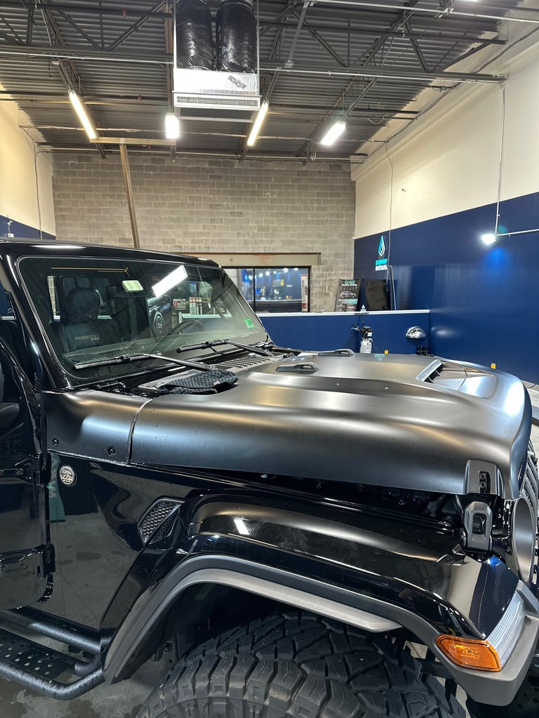 Black Jeep with hood open displaying custom stainless steel fuel tank in auto shop with blue accent wall