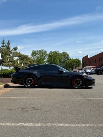 Black sports car parked in a lot with red brake calipers, trees and buildings in the background under a blue sky