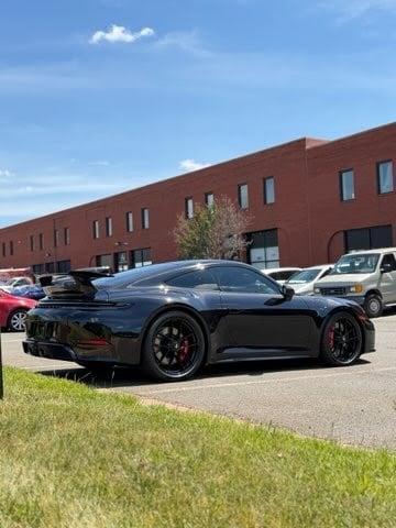 Black sports car parked in lot with red brick building and other vehicles in background