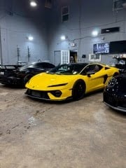 Bright yellow sports car parked in an indoor garage with dark vehicles visible in the background