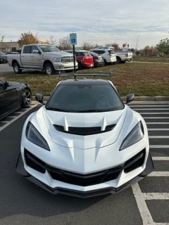 White sports car with aggressive front design parked in a lot with other vehicles in background